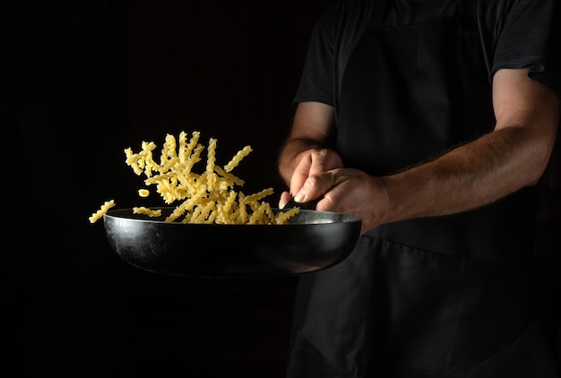 Cozinhar aletria na cozinha de um restaurante ou hotel O cozinheiro joga comida em uma panela quente Lugar para publicidade em um fundo escuro