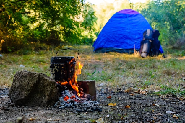 Cozinhar alimentos em uma chaleira na fogueira na floresta. Tenda no fundo