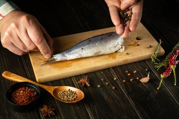 Foto cozinhar arenque em conserva com especiarias aromáticas pelas mãos de um cozinheiro na mesa da cozinha conceito de dieta de peixe em fundo escuro