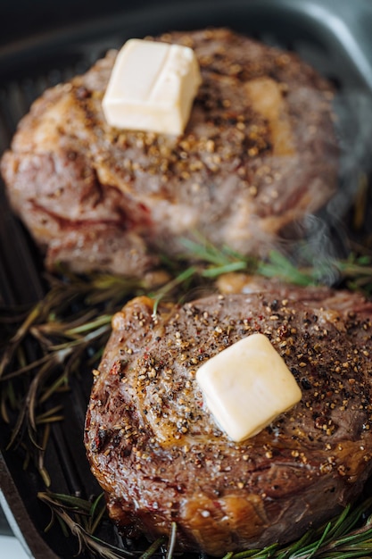 Cozinhar bifes suntuosos em uma assadeira com manteiga espalhando sobre o bife temperado com pimenta e sal com raminhos de alecrim