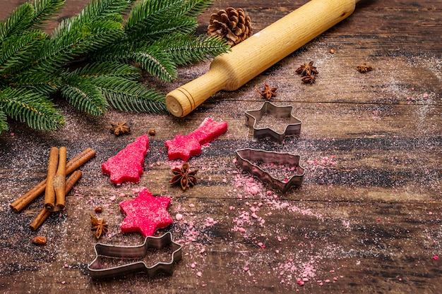 Cozinhar biscoitos de gengibre vermelho. Doces tradicionais de Natal. Árvore do abeto, especiarias, cortadores de biscoito, massa crua, rolo, tábuas de madeira