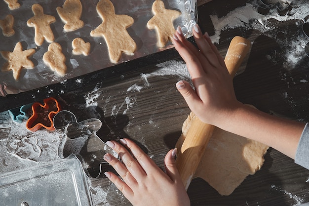 Cozinhar biscoitos de natal na mesa de madeira marrom escura. família fazendo homem-biscoito, cortando biscoitos de massa de pão de gengibre, vista de cima.