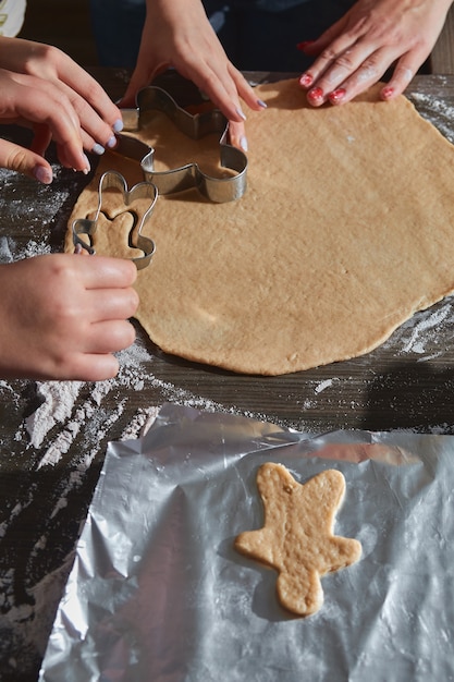 Cozinhar biscoitos de Natal na mesa de madeira marrom escura. Família fazendo homem-biscoito, cortando biscoitos de massa de pão de gengibre, vista de cima.