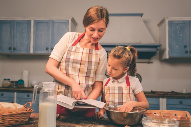 Foto cozinhar bolos caseiros. família amorosa feliz está preparando padaria juntos. mãe e filha filha menina estão cozinhando biscoitos e se divertindo na cozinha. procurando receitas em um livro de culinária