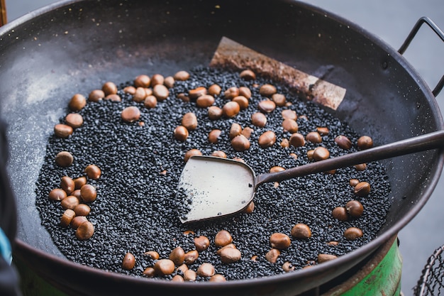 Cozinhar castanhas com a pedra quente na bandeja para a venda no mercado da porcelana.