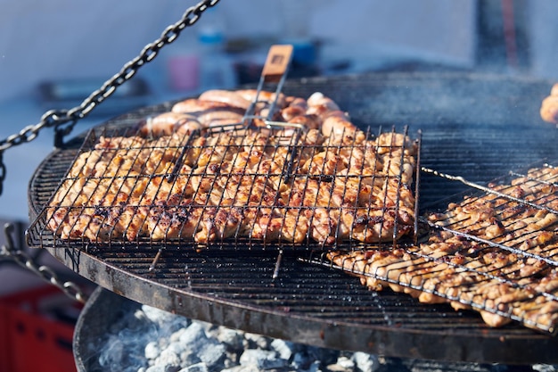 Cozinhar churrasco de frango na cesta de churrasqueira com cabo de madeira e deliciosa fumaça