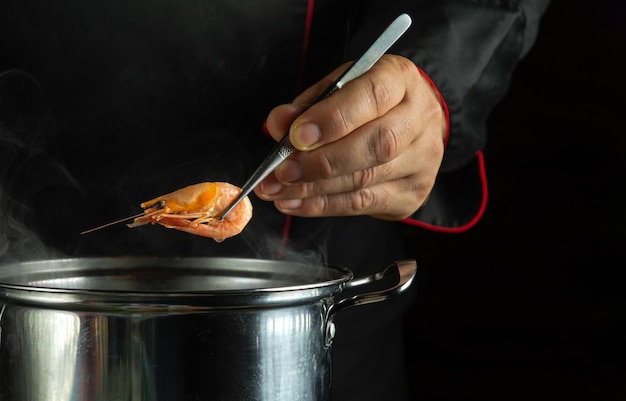 Foto cozinhar deliciosos camarões pelas mãos do chef na cozinha do restaurante o cozinheiro na mão segura um camarão cozido