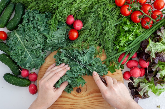 Cozinhar em casa o processo de cozinhar comida vegana saudável, as mãos das mulheres cortam a grama em uma placa de madeira.