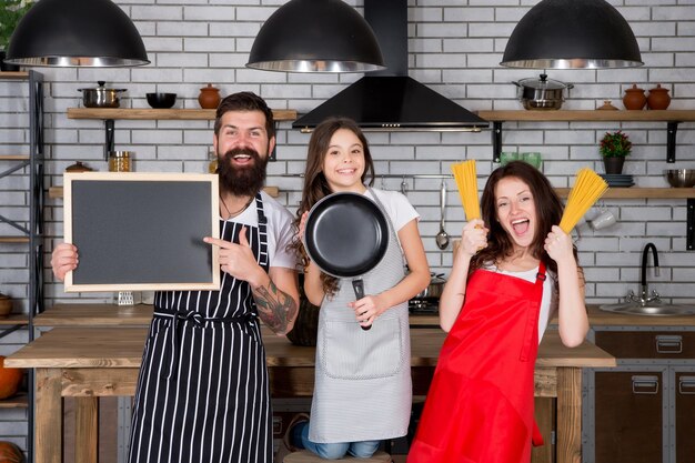 Cozinhar juntos. Espaço de cópia de receita. Conceito de restaurante familiar. Melhor equipe de cozinha. Mãe pai e filha aventais na cozinha. Hora do almoço. Família se divertindo cozinhando juntos. Ensine a criança a cozinhar.