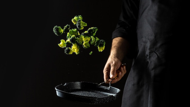 Cozinhar legumes frescos no chef da panela congelar o movimento de uma nuvem no ar no menu do restaurante preto dieta do livro de receitas