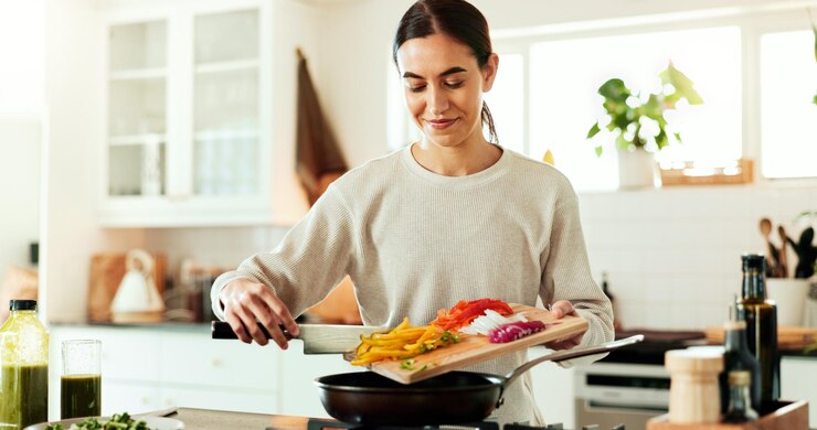 Foto cozinhar mulher e fogão de cozinha com legumes comida saudável e relaxar em casa com sorriso no balcão dieta nutrição e tábua de cortar com preparação de refeições feliz e brunch com saúde e bem-estar