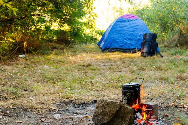 Cozinhar na fogueira na barraca de acampamento e mochila no fundo