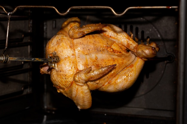 Cozinhar o frango no forno ou no espeto rotativo no espeto da grelha. Comida caseira.