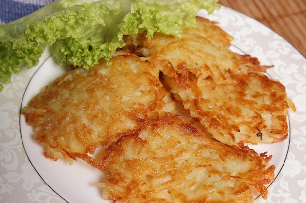 Cozinhar panquecas de batata caseiras com salada verde em um prato branco sobre um fundo de madeira Conceito de comida vegetariana Closeup