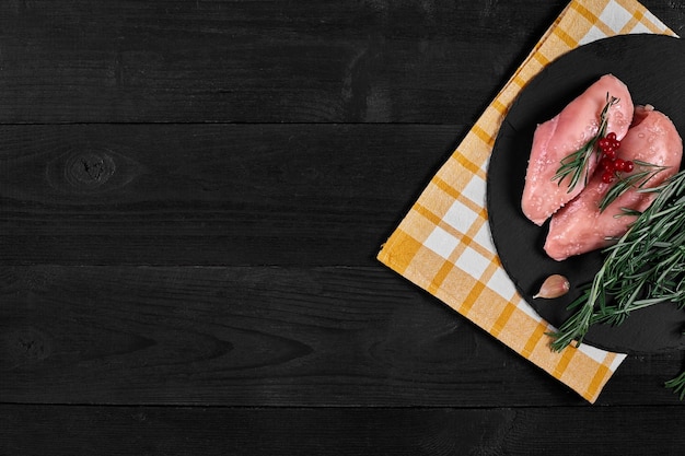 Cozinhar peitos de frango na mesa estão especiarias alecrim pimenta vermelha e preta conceito de comida saudável em um fundo de madeira preto vista superior com espaço de cópia natureza morta postura plana