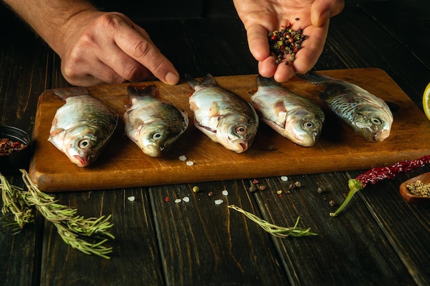 Cozinhar peixe Carassius marinado com especiarias aromáticas pelas mãos de um cozinheiro em uma tábua de corte Conceito de cozinhar peixe crucian na mesa da cozinha