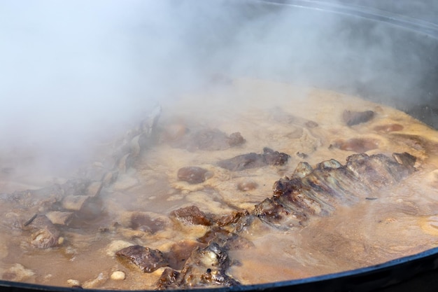 Cozinhar pilaf uzbeque real Assar costelas de cordeiro em um enorme caldeirão com muito vapor do lado de fora durante um festival folclórico tradicional