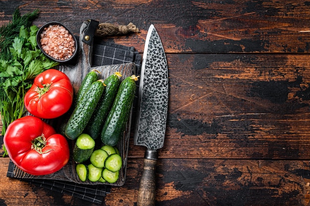 Cozinhar salada de vegetais verdes com tomate, pepino, salsa, ervas. fundo de madeira escuro. vista do topo. copie o espaço.