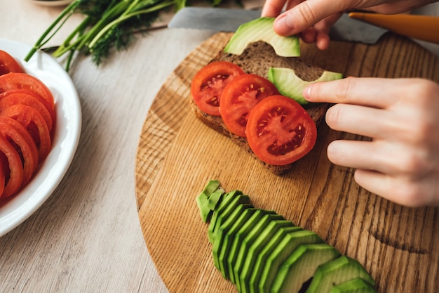 Cozinhar sanduíche saudável com abacate e tomate em casa na cozinha.