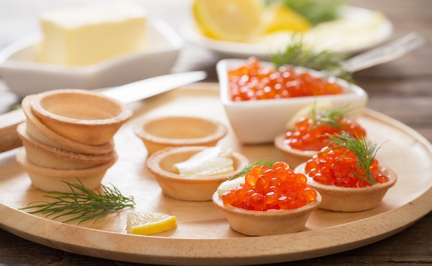 Cozinhar tortinhas com caviar vermelho na mesa de madeira