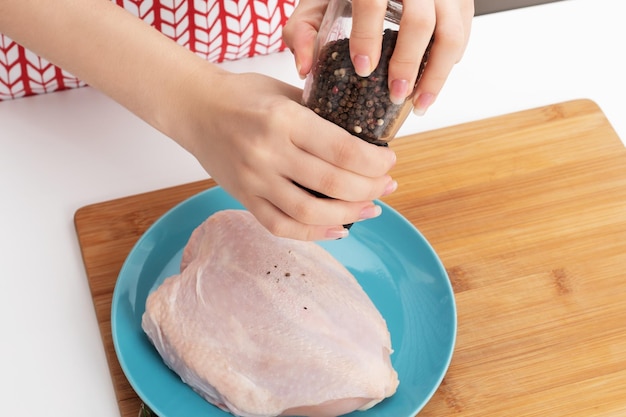 Cozinhar um delicioso jantar de dieta Mãos femininas adicionam especiarias ao peito de frango cru