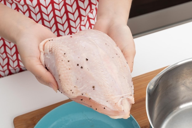 Cozinhar um delicioso jantar de dieta Mãos femininas colocam peito de frango cru em uma panela