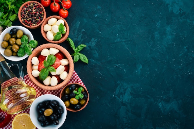 Cozinhar uma salada caprese Queijo mussarela tomate cereja azeitonas folhas de manjericão óleo pimenta Em uma mesa de pedra preta Espaço livre para texto