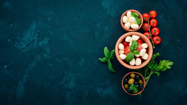 Cozinhar uma salada caprese Queijo mussarela tomate cereja azeitonas folhas de manjericão óleo pimenta Em uma mesa de pedra preta Espaço livre para texto