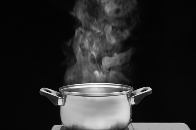 Cozinhe a vapor na panela na cozinha em fundo escuro