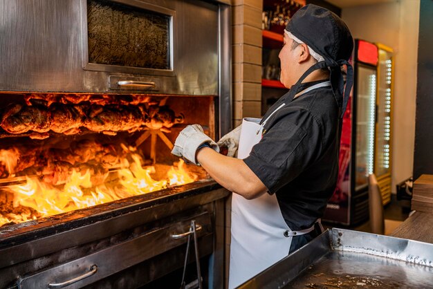 Cozinhe atiçando o fogo para cozinhar pilha de frango grelhado em um espeto