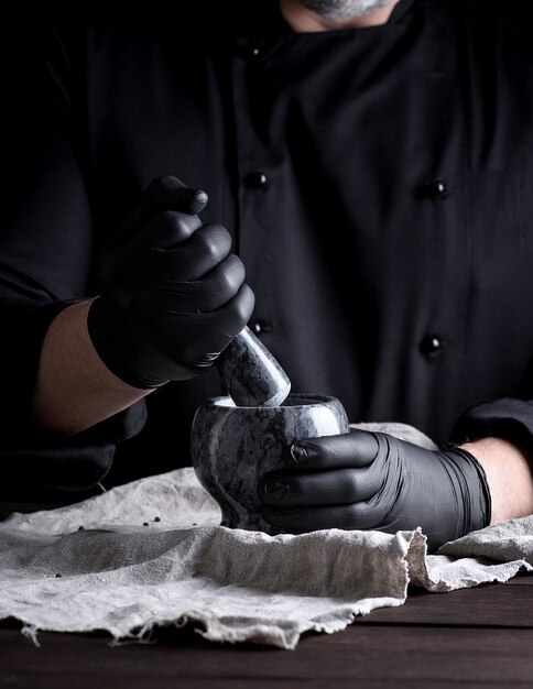 Cozinhe em luvas de látex pretas, segurando um almofariz de pedra com pimenta