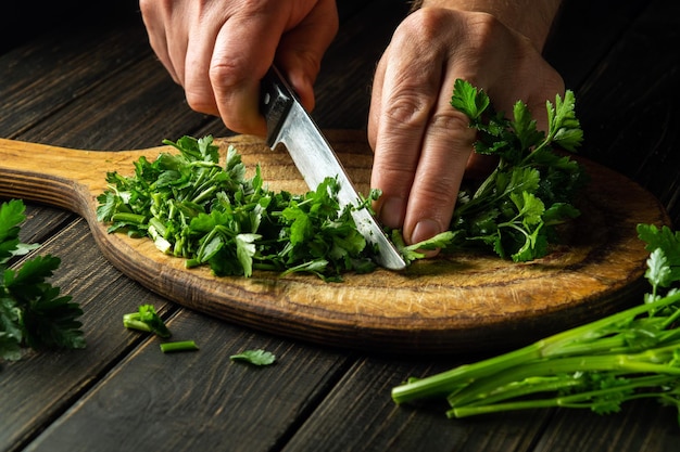 Cozinhe o corte de salsa verde em uma tábua de corte com uma faca