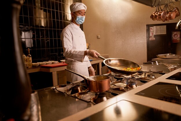 Foto cozinheiro asiático inclinando uma panela quente com fatias de vegetais