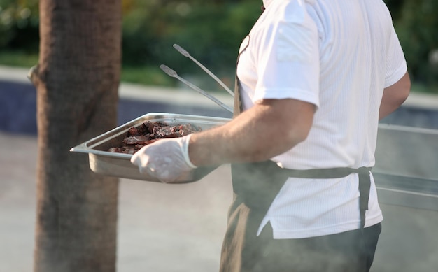 Cozinheiro carrega assadeira com carne grelhada