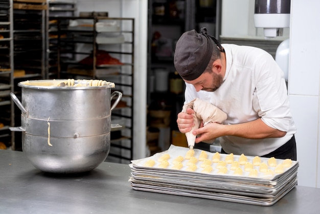 Cozinheiro chefe da pastelaria com o creme de espremedura do saco dos confeitos na loja de pastelaria.