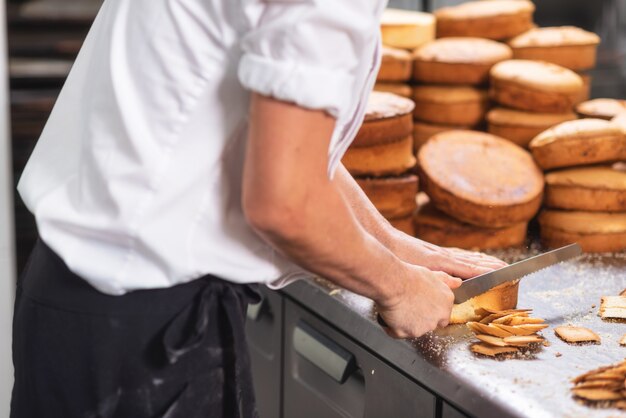 Foto cozinheiro chefe de pastelaria que corta o bolo de esponja em camadas. processo de produção de bolo.