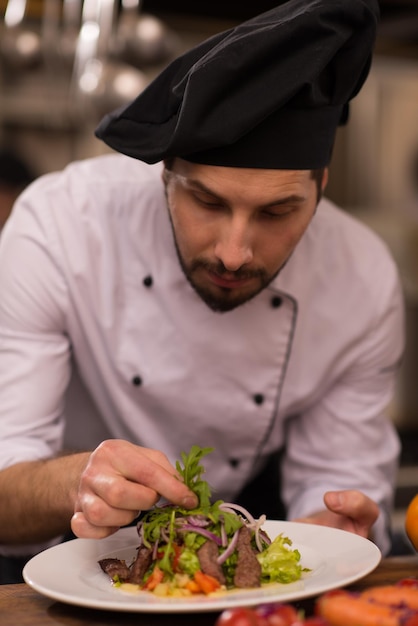 cozinheiro chefe decorando o prato de refeição preparada no prato na cozinha comercial do restaurante