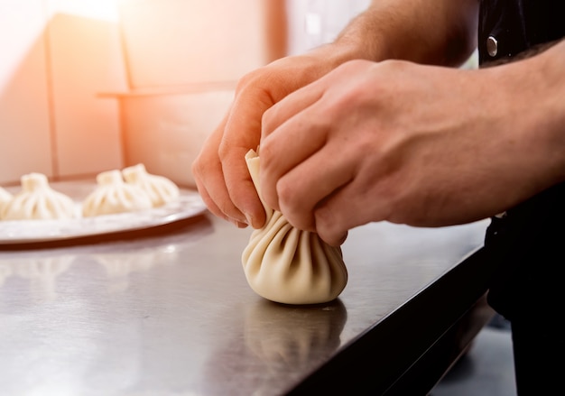 Foto cozinheiro chefe que coocking o khinkali georgian ou o wonton japonês. refeição tradicional de massa e carne. cozinha nacional, processo de cozimento. cozinha de restaurante.