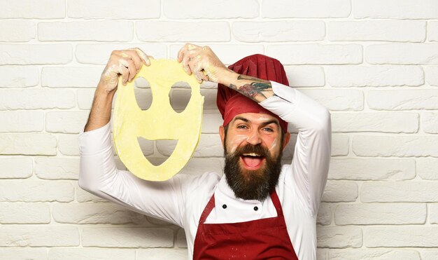 Foto cozinheiro com cara animada em uniforme borgonha brinca com massa