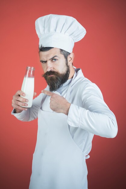 Cozinheiro de bebidas saudáveis com uma garrafa de leite mostra o dedo no chef com uma cara séria no chapéu branco