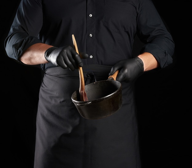 Cozinheiro de uniforme preto e luvas de látex segurando uma panela redonda vazia de ferro fundido preto