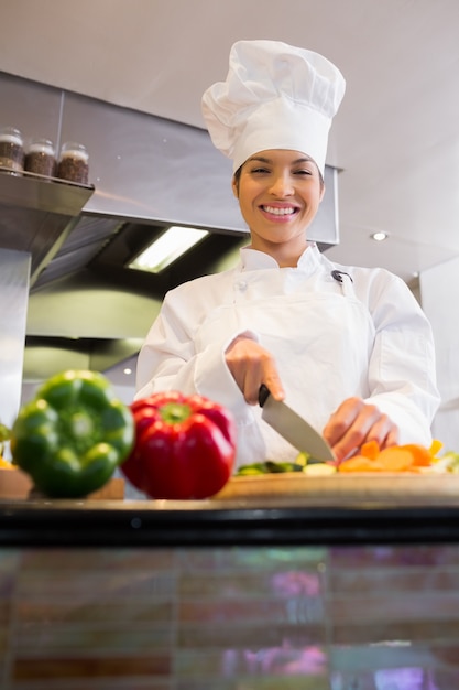 Cozinheiro feminino sorrindo cortando vegetais na cozinha