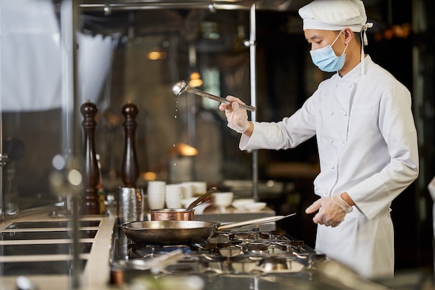 Cozinheiro habilidoso com máscara facial segurando uma concha sobre uma panela