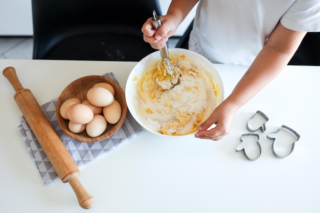 Cozinheiro infantil agita a massa para biscoitos com um batedor