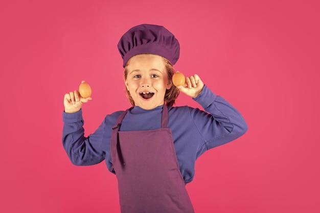 Cozinheiro infantil segura ovos Cozinhando crianças Chef garoto em forma de cozinheiro Menino com avental e chapéu de chef preparando uma refeição saudável no fundo isolado do estúdio Processo de cozimento