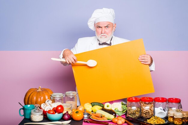 Cozinheiro maduro de homem posando de avental de cozinha. Ótima receita. Cozinheiro-chefe e culinária profissional. Cozinheiro chefe sênior. Cozinheiro chefe do retrato com sinal de mão no fundo do quadro-negro. Chefcook mostrando no texto.