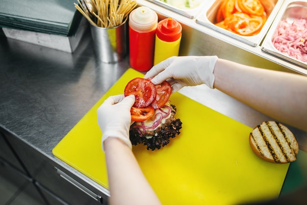 Cozinheiro põe tomates no hambúrguer