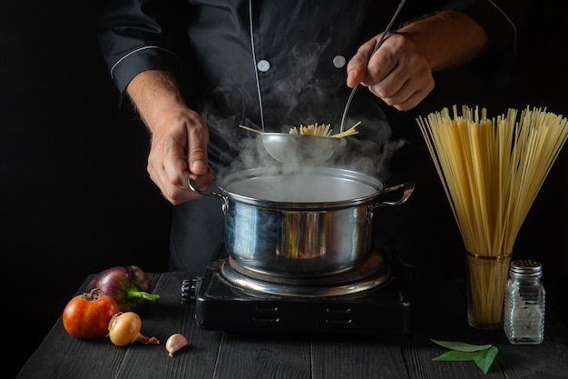 Cozinheiro prepara macarrão italiano em uma panela com legumes Closeup de mãos de cozinheiro enquanto cozinha