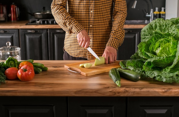 Cozinheiro segura a faca na mão e corta na tábua de cortar abobrinha verde para salada
