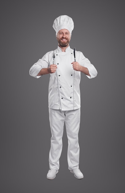 Cozinheiro sorridente em uniforme de chef com garfo e faca